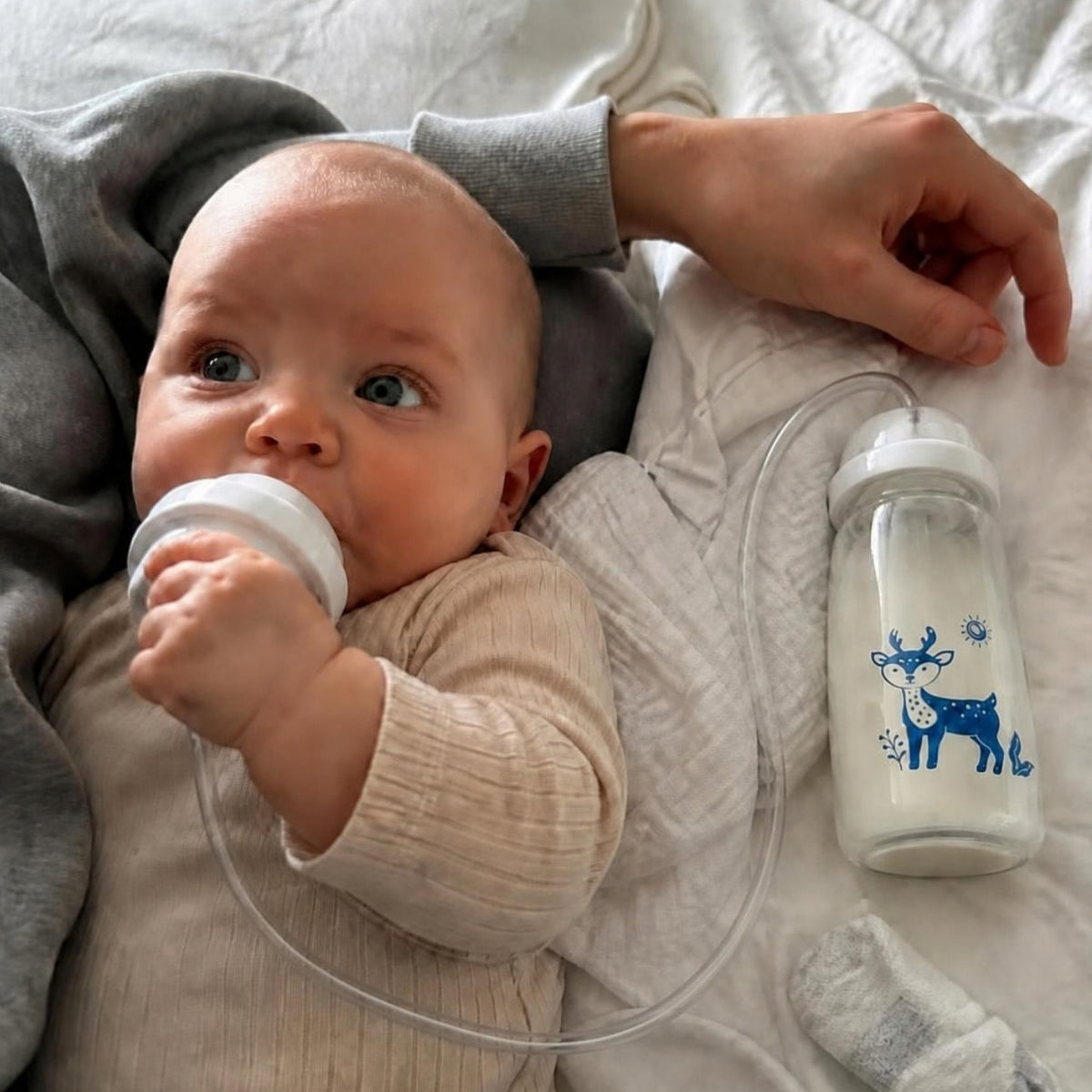 Baby trinkt mit der Freihand-Babyflasche, ein Erwachsener ist direkt daneben